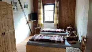 Zimmer der Ferienwohnung mit zwei Einzelbetten, Holzwand am Fenster und Kleiderschrank aus hellem Holz